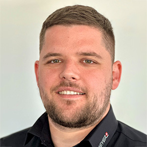 Mann mit kurzen braunen Haaren und gepflegtem Bart lacht, trägt schwarzes Hemd, neutraler Hintergrund, Blechbearbeitung-Experte.