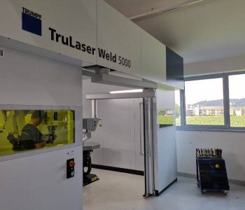 TruLaser Weld 5000 in heller Industriehalle; Person bedient Maschine hinter gelbem Fenster. Werkzeuge bei großen Fenstern.