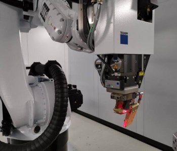 Nahaufnahme eines Roboterarms mit TRUMPF Laser-Schneidkopf in Industrieumgebung, Kabeln und Blechbauteilen sichtbar.