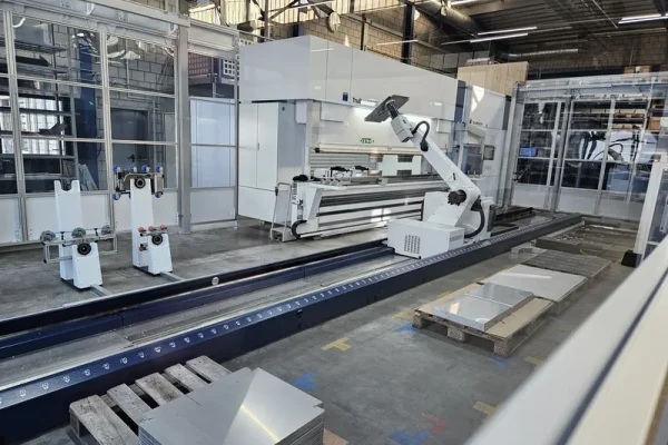 Eine moderne Industriehalle mit weissem Roboterarm, der bei der Blechbearbeitung vor Glaswänden und LED-Licht arbeitet.