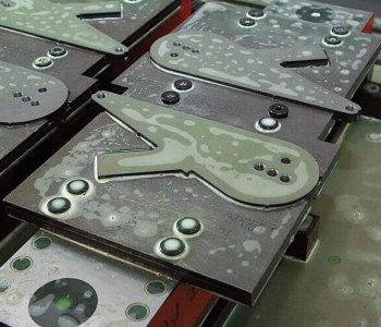 Nahaufnahme von Metallblechen mit Vögel-Formstanzungen, Schraubbolzen und Markierungen, nass in einer Blechbearbeitungswerkstatt.