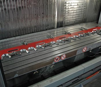 CNC-Maschinenbett mit langem roten Metallwerkstück, mehrfach gespannt; Innenfläche gerippt, Keineintrittsschild sichtbar.