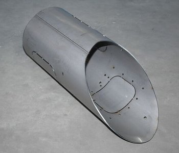 Glänzendes, zylindrisches Blechbauteil mit rundem, offenem Ende und Bohrungen liegt auf grauem Betonboden.