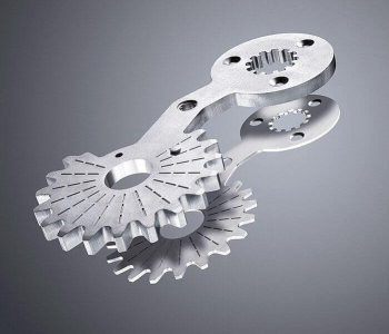 Zwei ineinandergreifende, silberfarbene Metallzahnräder an gelochter Blechplatte, Reflexionen auf glatter grauer Fläche.