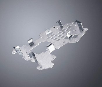 Ein metallisches, unregelmäßig geformtes Stanzteil mit Ausschnitten und Laschen auf grauem Farbverlauf-Hintergrund.