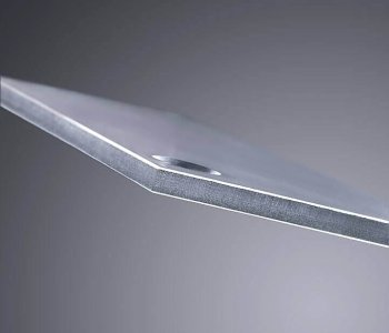 Detailansicht einer dünnen Metallblech-Kante mit Fase und Stanzloch, vor unscharfem grauem Hintergrund.