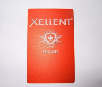Rote Blechkarte mit XELLENT oben, darunter Schild mit weissem Kreuz und Text swiss made swiss vodka, geprägt und mattiert.