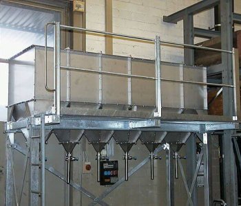 Großer Metall-Trichter mit mehreren Trichtern auf Rahmen, Geländer und Steuerung in Blechlagerhalle mit Backsteinwänden.