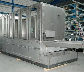 Ein grobes, unfertiges Metallfahrgestell steht in einer Werkhalle, umgeben von Werkzeugen und Material für Blechbearbeitung.