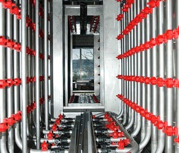 Reihen von Metallrohren mit roten Ventilen bilden in einer Industriehalle einen symmetrischen Rohrleitungsdurchgang.