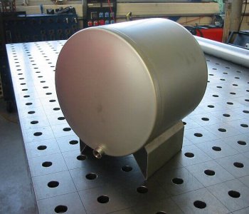 Zylindrischer Metallbehaelter mit Auslassrohr auf Lochblechtisch, montiert auf Ständer, umgeben von Werkstattwerkzeugen.