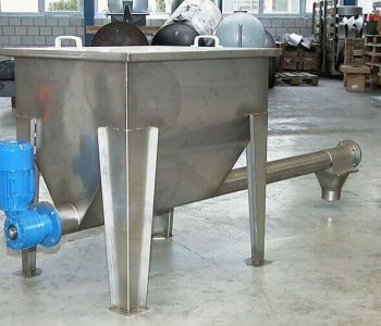 Edelstahlindustrie-Trichter mit blauem Motor, schrägen Beinen und Schneckenförderer in einer Werkhalle mit Paletten und Maschinen.