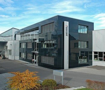 Modernes Industriegebäude mit Glasfassade "METTLER TOLEDO", umgeben von Pflaster, Grün und Blechbearbeitungs-Kompetenz.