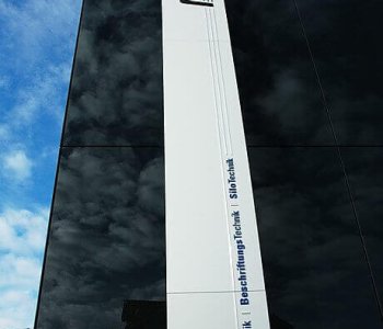 Modernes Hochhaus mit dunklen Glasfassaden, MEYER-Logo und Blechbearbeitung-Service, vor blauem Himmel mit Wolken.