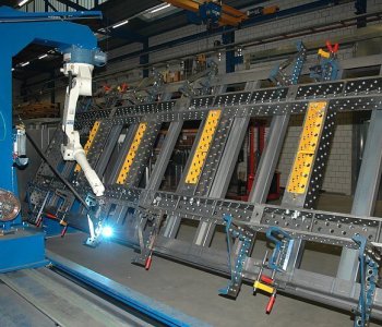 Ein Industrieroboter schweißt an einer großen, teilmontierten Metallstruktur in einer Fabrikhalle für Blechbearbeitung.